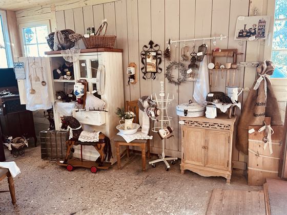 Helle Landhaus-Vitrine mit Textilien, davor ein kleines Schaukelpferd